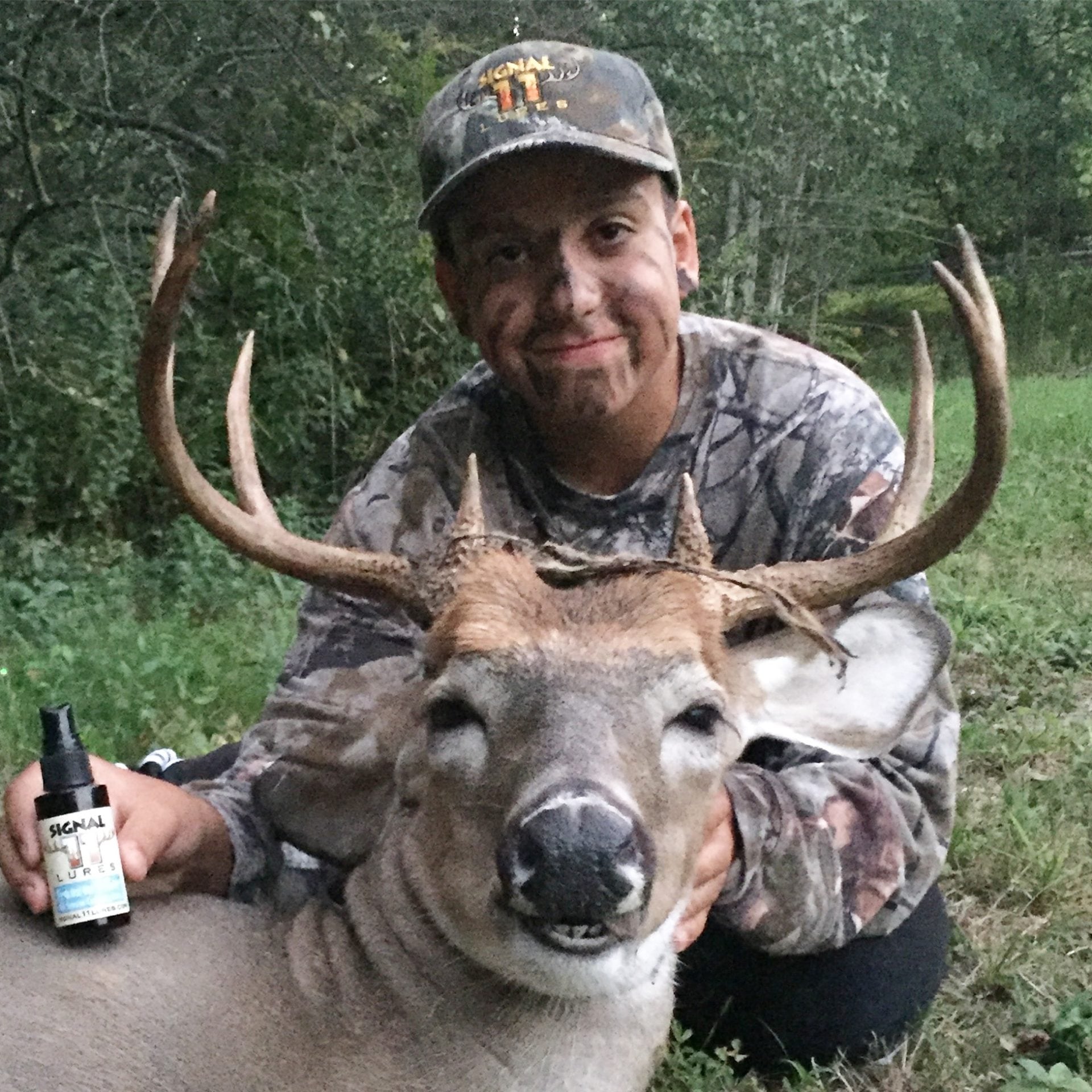 A man holding a beer in his hand while sitting next to a deer.