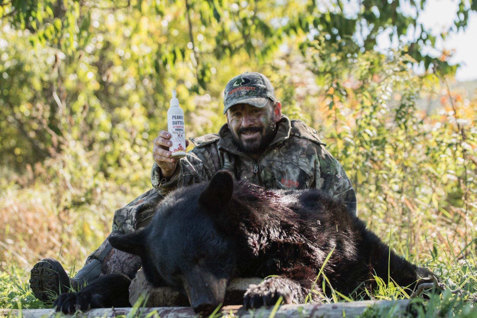 A man in camouflage holding a knife and sitting next to a bear.