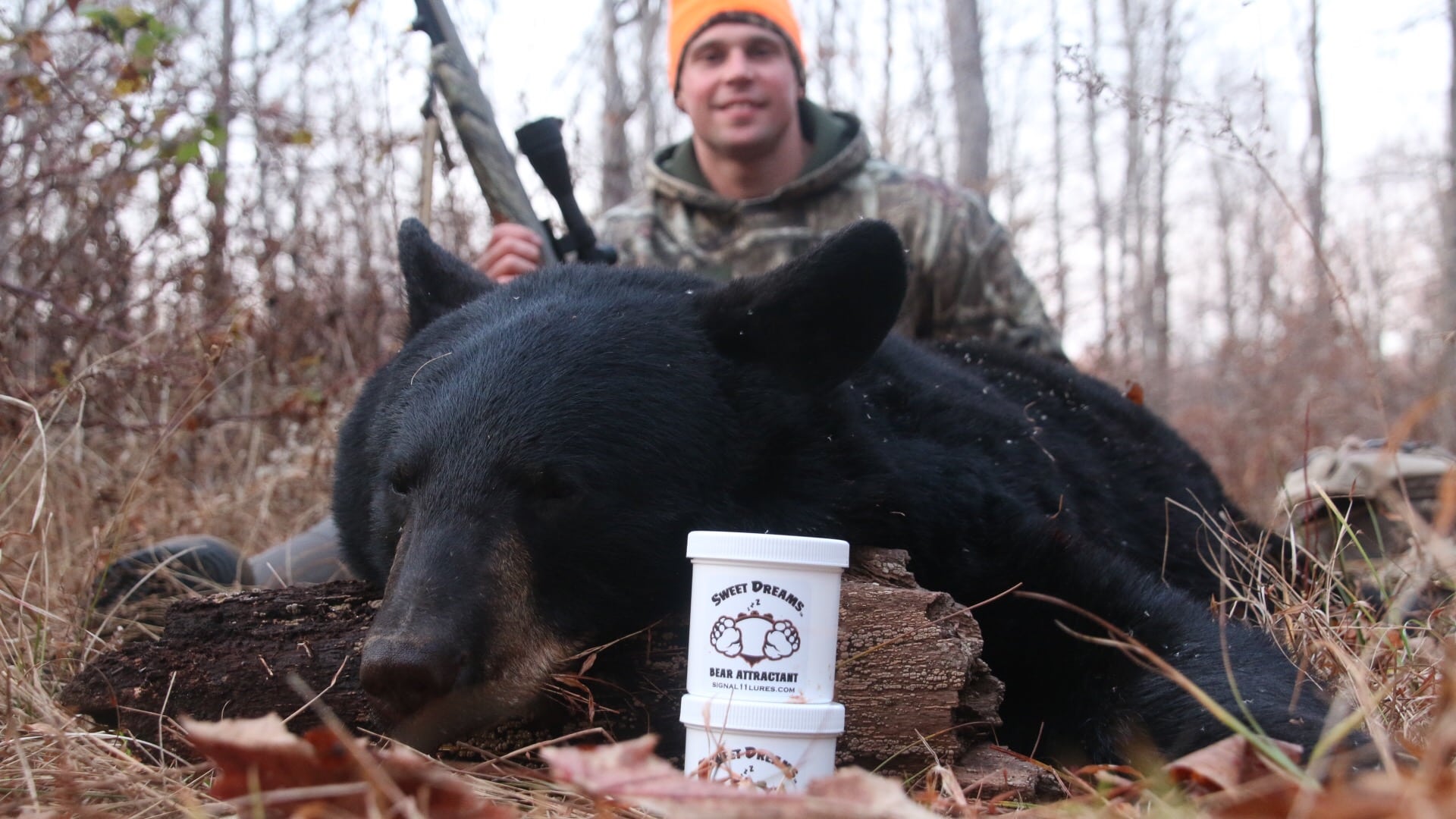 A man with a rifle and bear in the woods.