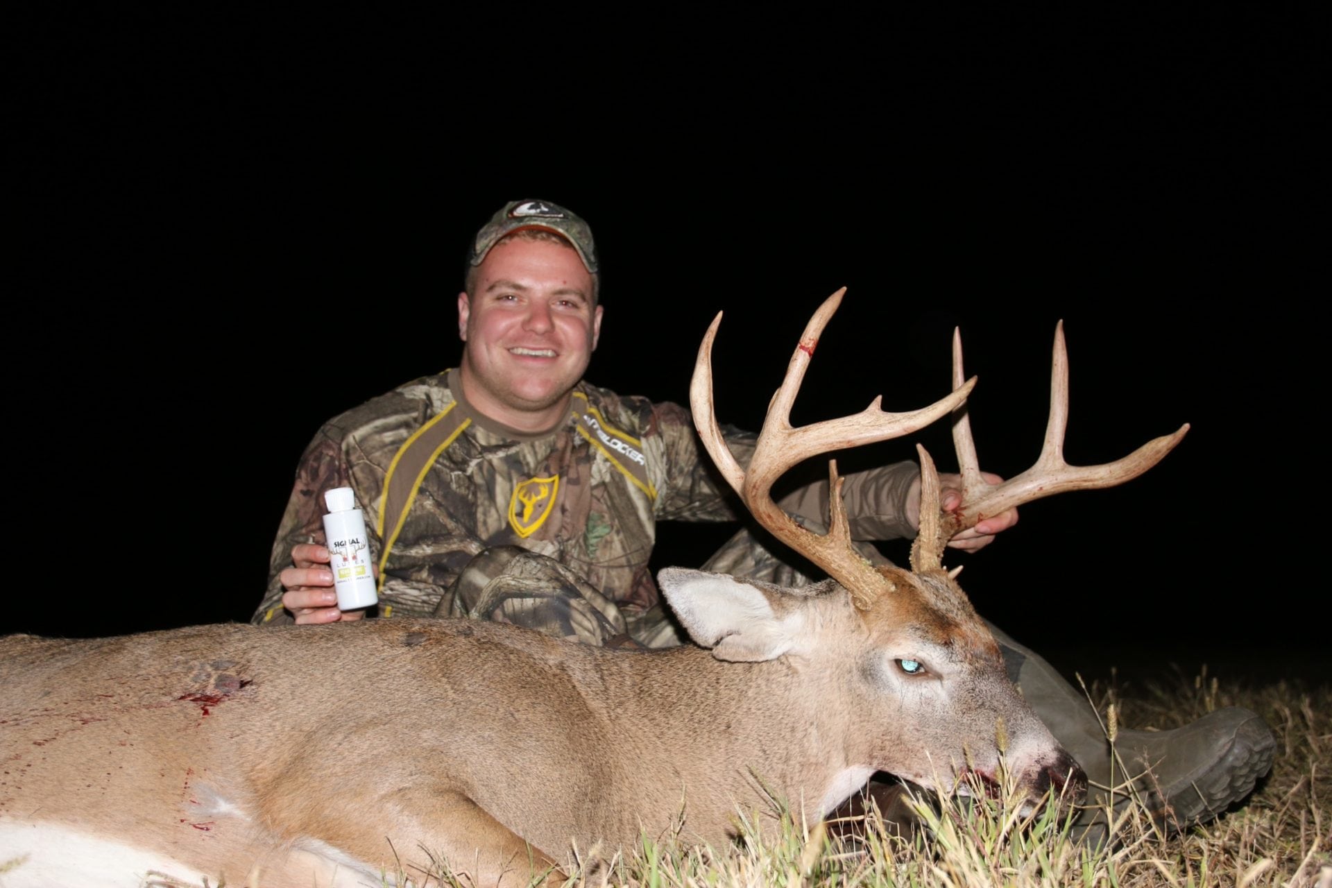 A man holding a bottle of beer next to a deer.