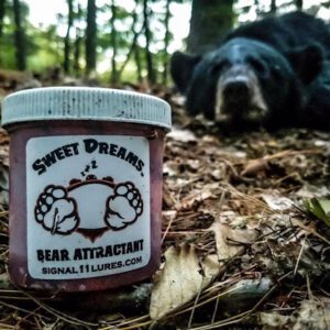 A bear laying in the woods next to a jar of jam.