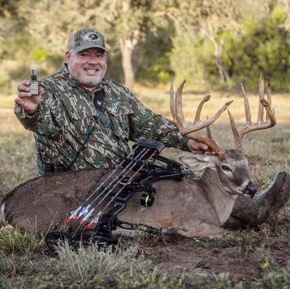 A man in camouflage sitting next to a dead deer.